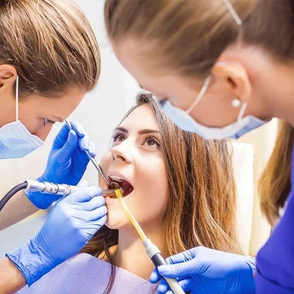 Dental professionals in gloves examine a young adult patient's teeth in a bright clinical setting