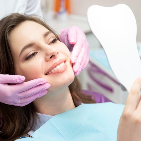Smiling patient checking her teeth in a hand mirror held by the dentist